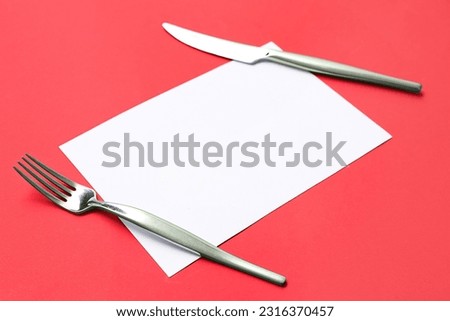 Blank card, stainless steel fork and knife on red background, closeup