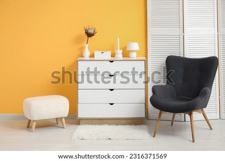 Dark grey armchair with dressing screen, dresser and fluffy rug near orange wall Royalty-Free Stock Photo #2316371569