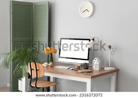 Stylish workplace with modern PC and narcissus flowers near light wall Royalty-Free Stock Photo #2316372073