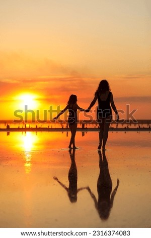 Happy family summer travel holiday. Silhouette of mom with child daughter holding hands walking together on beach on sunset. Happy mothers day. Concept of family values. International Children's Day.