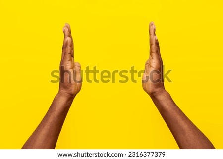 two hands of african american man hold empty space on yellow isolated background, guy shows the size with his hands, close-up Royalty-Free Stock Photo #2316377379