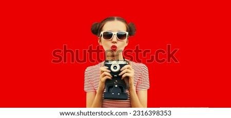 Portrait of happy young woman photographer with film camera, female with cool girly hairstyle on red background