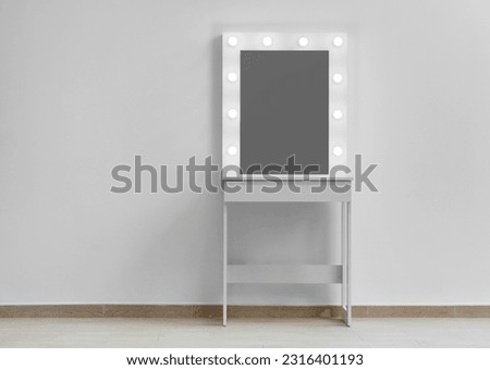 A white makeup dressing table with a large mirror and lights on against the wall. Makeup artist's workplace, modern dressing room. Royalty-Free Stock Photo #2316401193