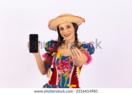 Young woman in typical June party clothes holds a cell phone with a blank screen for texting, invites you with her hand