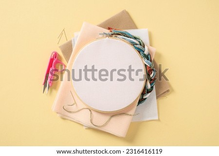 Embroidery concept. Flat lay frame with blank canvas and needlework accessories on pastel yellow background