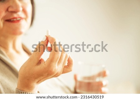 Close up of a retired woman in casual clothes at home holding pill and glass water. 
