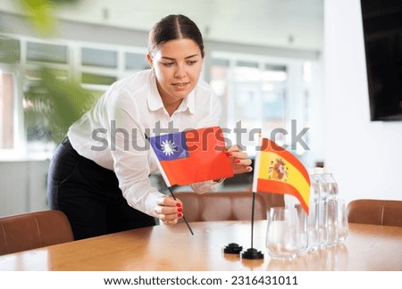 Young woman in business clothes puts flags of Taiwan and Spain on negotiating table in office