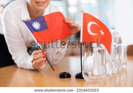 Woman secretary prepares an office for negotiations - she places flags of Taiwan and Turkish the table
