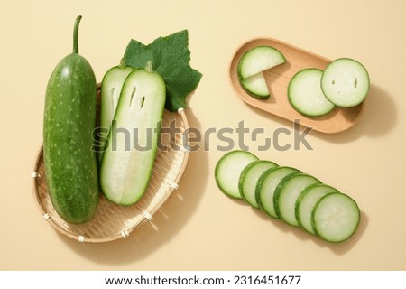 Scene for advertising product with winter melon (Benincasa hispida) ingredient. Fresh winter melon, some slices and green leaf are placed on bamboo basket and wooden plate on beige background Royalty-Free Stock Photo #2316451677
