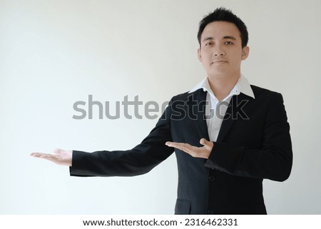 Young Asian business man opening his both palm hands to his right side and looking to the camera