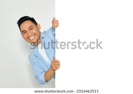Portrait of happy young Asian man in casual clothes hiding behind blank white billboard for mockup template isolated on white background Royalty-Free Stock Photo #2316462511