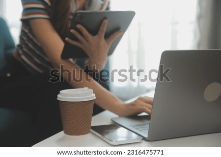Happy Asian teen girl holding pad computer gadget using digital tablet technology sitting on the couch at home. Smiling young woman using apps, shopping online, reading news, browsing internet on sofa