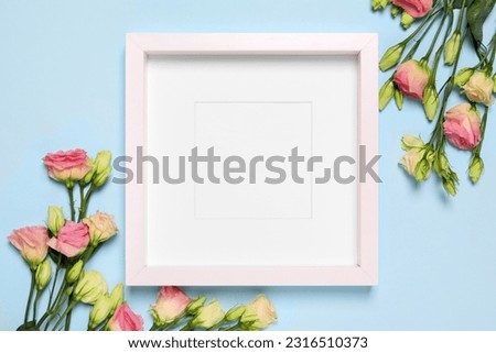 Empty photo frame and beautiful flowers on light blue background, flat lay. Space for design