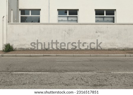 White weathered surrounding wall with white building on behind. Sidewalk and asphalt road in front, Background for copy space. Royalty-Free Stock Photo #2316517851