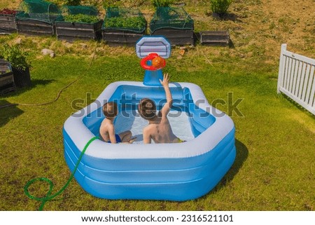 Two boys in inflatable outdoor swimming pool playing water basketball on backyard on sunny summer day. Sweden.