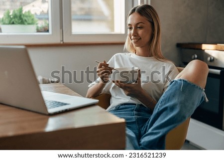 Yong woman using laptop in the morning while having breakfast. Royalty-Free Stock Photo #2316521239