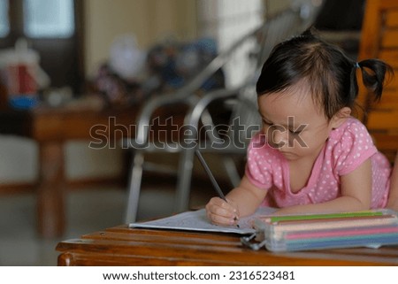 Little asian girl was coloring cartoons on coloring book at home. Coloring Book Education Talent Concept. Copy space.