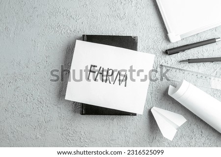 Top view of FARM writing on white sheet on black notebook pens ruler paper plane desk blank on gray sand background