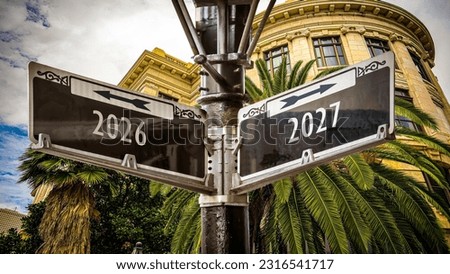 An image with a signpost pointing in two different directions in German. One direction points to 2027, the other points to 2026. Royalty-Free Stock Photo #2316541717
