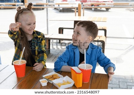 Happy children girl and boy brother and sister eat nuggets and french fries at fast food restaurant. Unhealthy meal for kids. Junk food. Overweight problem child.