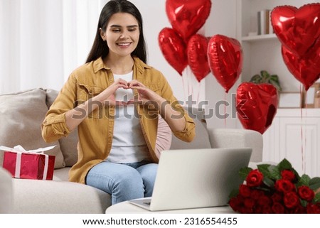 Valentine's day celebration in long distance relationship. Beautiful young woman making heart with hands while having video chat with her boyfriend via laptop Royalty-Free Stock Photo #2316554455