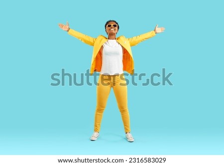 It finally happened. Joyful emotionally excited dark-skinned woman sincerely rejoices on light blue background. Full length of happy african american woman raising hands and looking up joyfully. Royalty-Free Stock Photo #2316583029