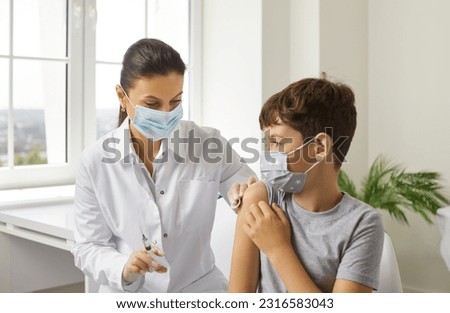 Female nurse in vaccination center vaccinates little boy against coronavirus or flu. Doctor and child in protective masks in medical office. Concept of childhood vaccination and immunization. Royalty-Free Stock Photo #2316583043