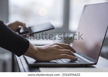 Woman's fingers nimbly typing on a cutting-edge laptop keyboard, with a blurred office scene behind