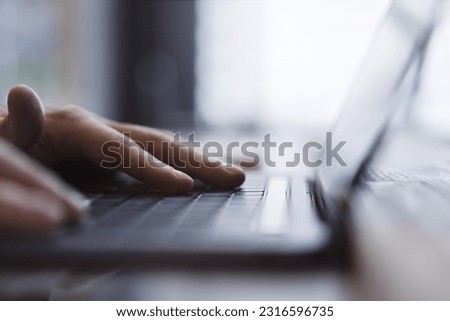 A man's hands are captured up close, busily typing on a sleek laptop keyboard, set against a fuzzy office background