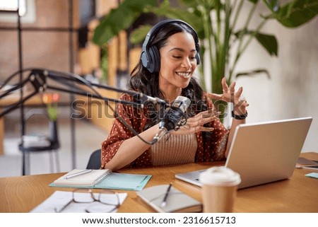 Beautiful radio host recording podcast in studio. Young mixed race woman recording a podcast in studio. Smiling multiethnic woman speaking on microphone over laptop at her home studio.