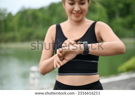 Close-up image of a beautiful and sporty Asian woman in sportswear checking her calories burned and running miles on her smartwatch after a run outdoors. Royalty-Free Stock Photo #2316616211
