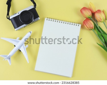 Top view or flat lay of blank page opened notebook, airplane model, digital camera and tulips flowers  on yellow  background with copy space.