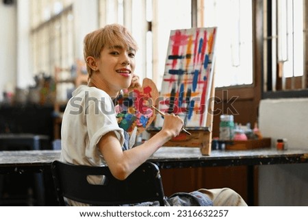 Happy young stylish man painting with watercolor on canvas in art workshop. Art, creative hobby and leisure activity concept
