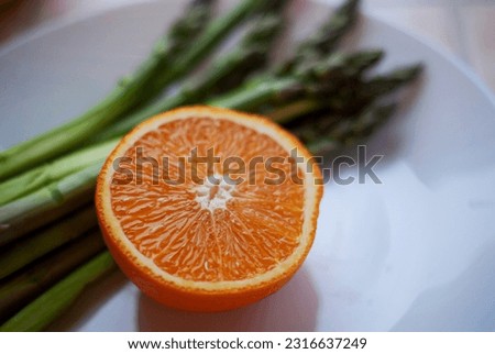 Fresh green asparagus and half an orange lie on a white plate. Conceptual photo: healthy lifestyle, healthy eating, organic food, vegetarianism, veganism.