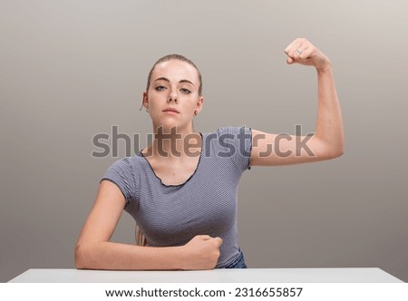 Strong young woman leans on forearm in a manly way and flexes other muscle, pulling it with fist. Her cocky and confident expression says she won't be ordered around, she's her own boss Royalty-Free Stock Photo #2316655857
