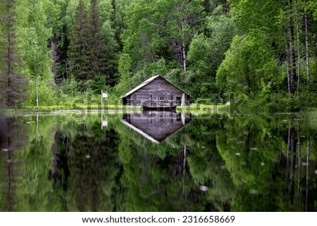 Old grain mill or watermill across the mill pond in summer in Kenozersky National Park, Arkhangelsk Oblast, Russia. Boat view from the water with reflection