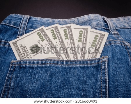Five 100 US dollar banknotes in a jeans pocket on a black background. Close-up photo. Money and Finance concept. Top view
