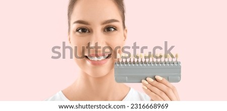 Beautiful young woman with teeth color samples on pink background