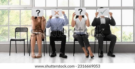 Young people hiding faces behind paper sheets while waiting for job interview  Royalty-Free Stock Photo #2316669053