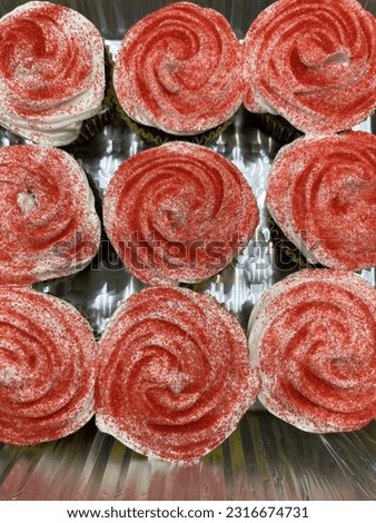 The top down view of a tray of cupcakes with vanilla frosting and red sprinkles.