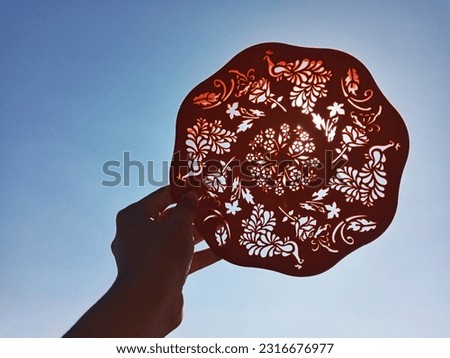 Silhouette of A Hand Holding Carved Plastic Plate Under Bright Blue Sky Background