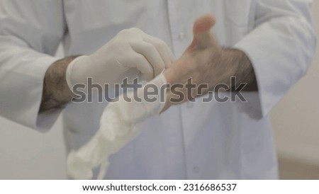 Doctor or nurse in white medical suit puts on protective gloves. Close-up. Concept of professional clinical care, uniform and healthcare.