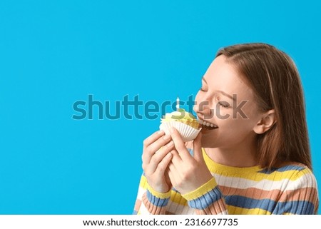 Beautiful young woman eating tasty birthday cake on blue background