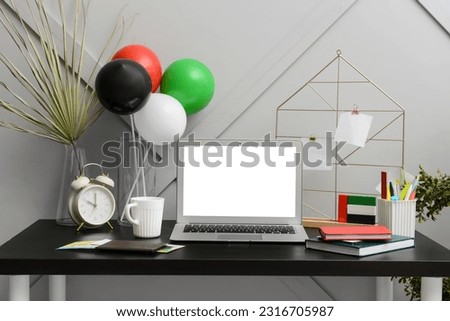Modern workplace with balloons and blocks in colors of UAE flag near light wall Royalty-Free Stock Photo #2316705987