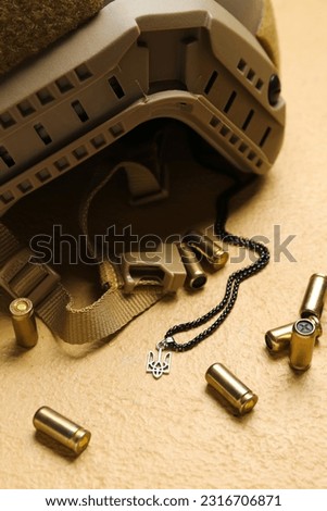 Military helmet, bullets and chain with Ukrainian coat of arms on beige background, closeup