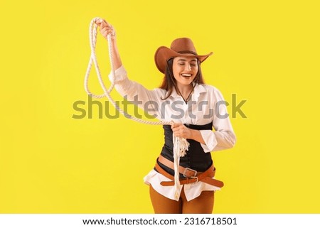 Beautiful cowgirl with lasso on yellow background Royalty-Free Stock Photo #2316718501
