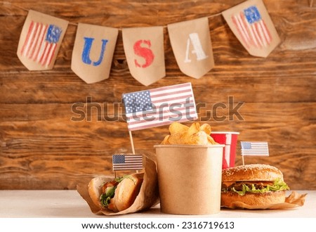 Tasty burger, potato chips, hot dog and cup of drink on table against wooden background. Memorial Day celebration