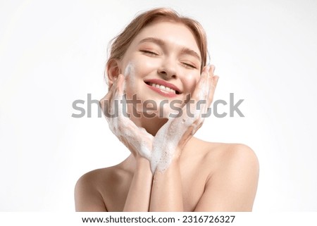 A happy young woman cleanses her skin with a gentle facial foam, the model applies the cleanser to her skin and smiles. Royalty-Free Stock Photo #2316726327