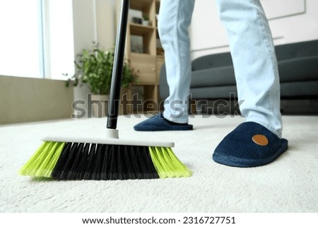 Young man sweeping carpet with broom at home, closeup Royalty-Free Stock Photo #2316727751