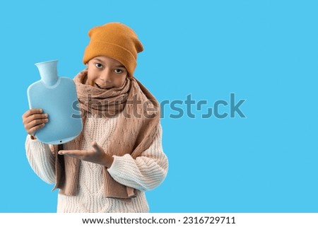Little African-American boy showing hot water bottle on blue background
